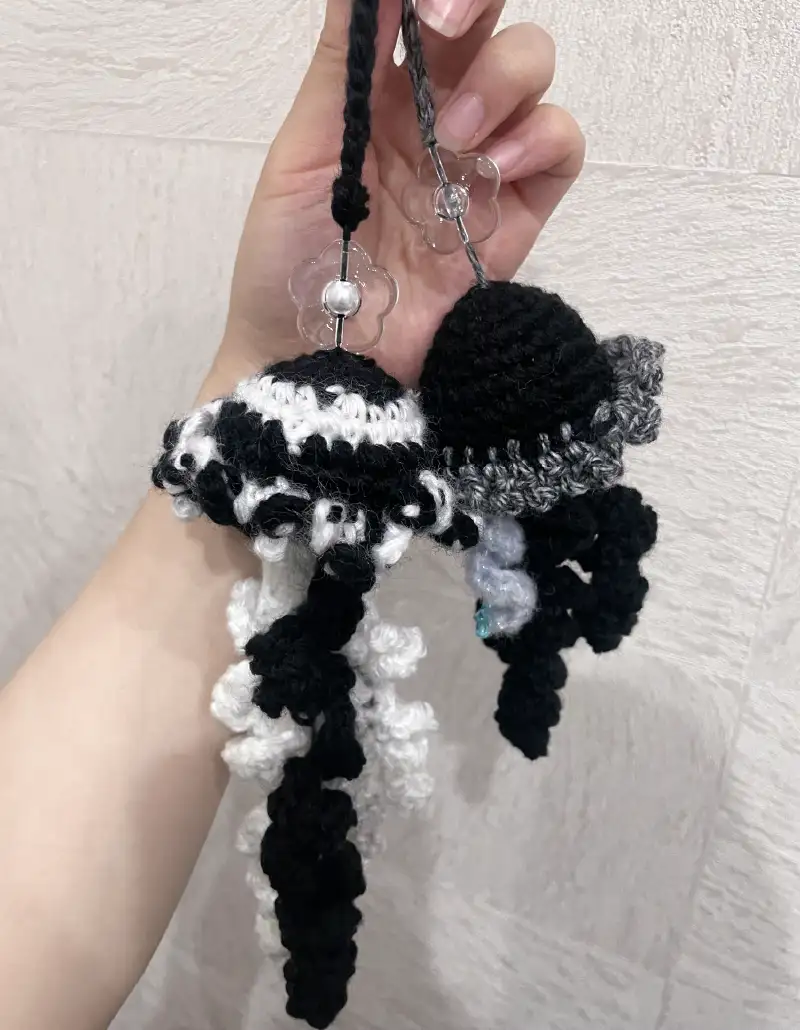 黒とグレーの毛糸で編まれたクラゲ型ストラップ。繊細に作られた触手と落ち着いた色合いが特徴。