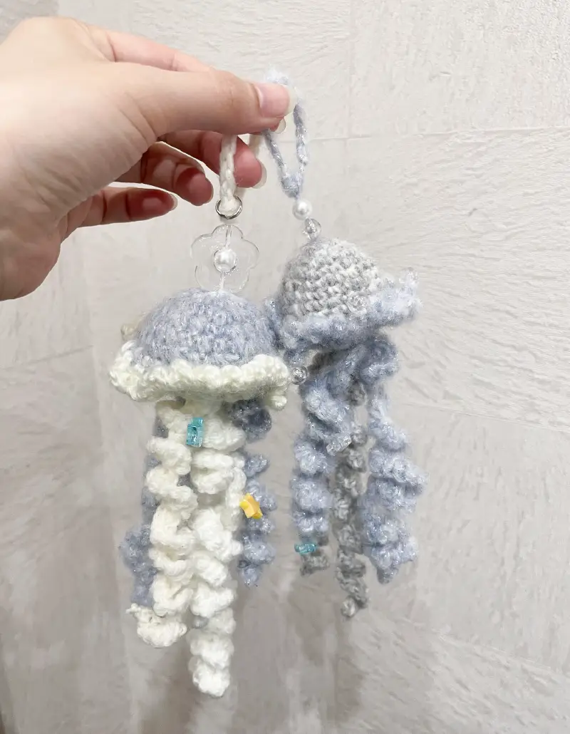 白と水色の毛糸で編まれたクラゲ型ストラップを手に持っている様子。ビーズがアクセントとして付いている。