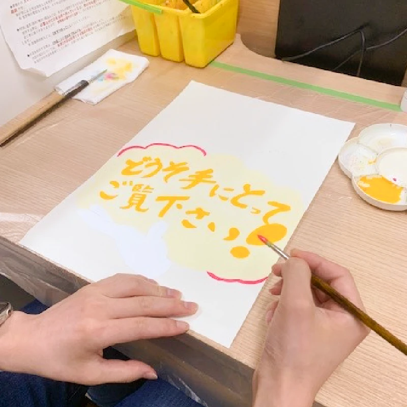 「どうぞ手に取ってご覧下さい」と描かれたPOPを筆で制作中