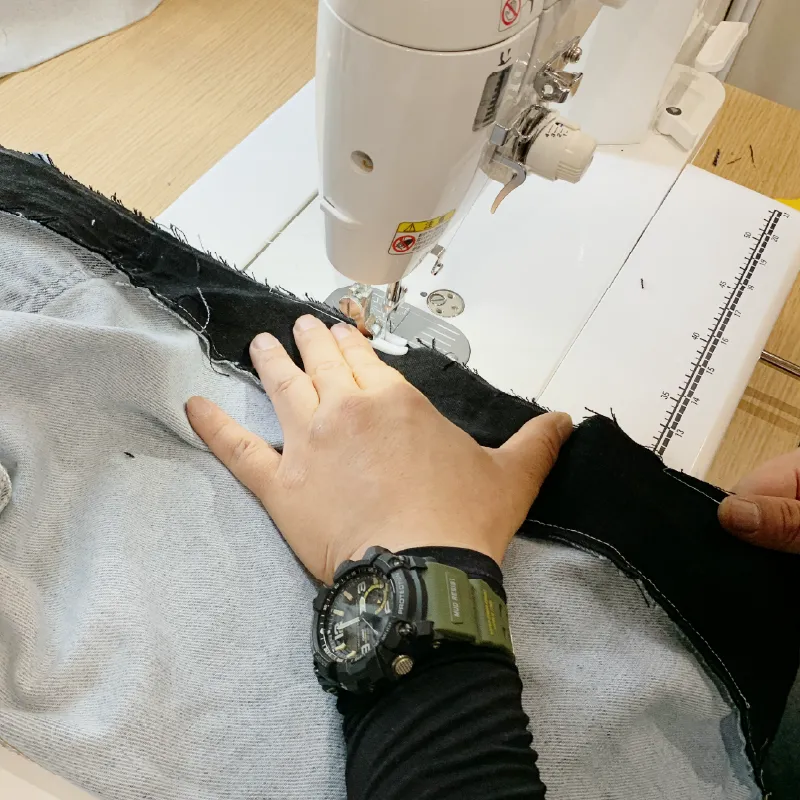 作業台に置かれたミシンと、デニムを縫い合わせる手元。