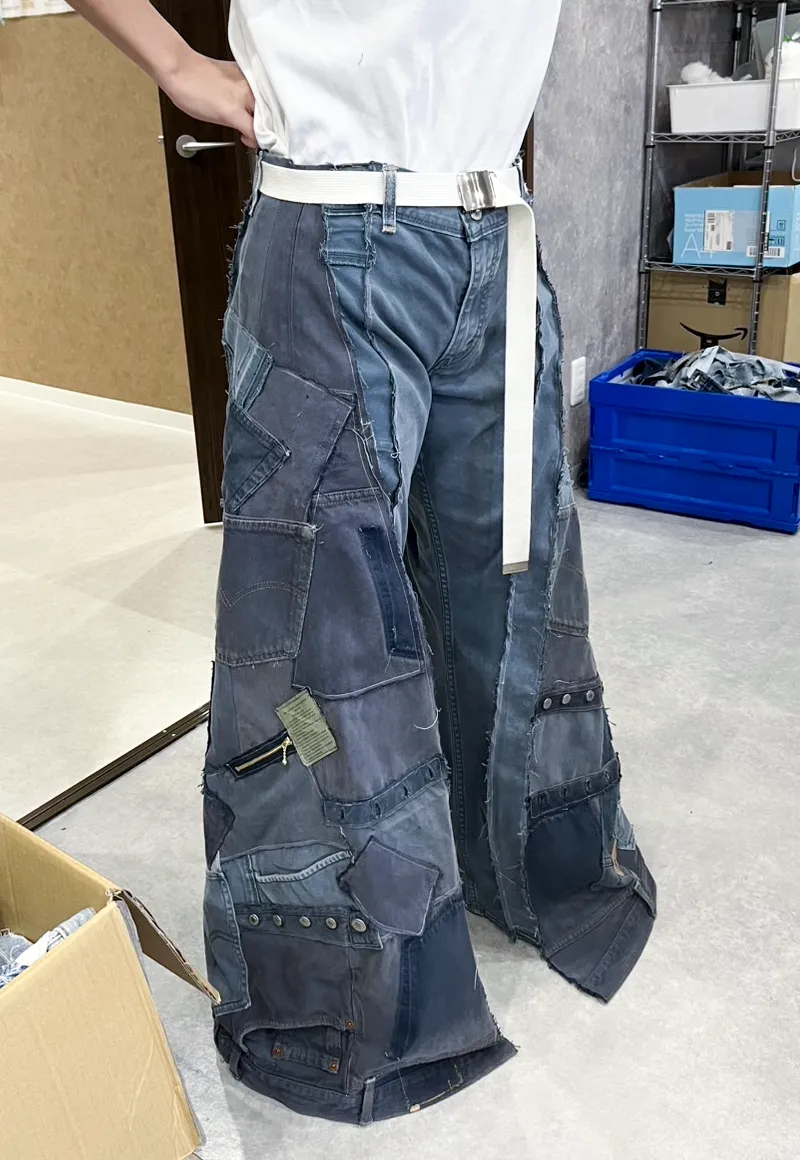 着古した複数のデニム生地をパッチワークで繋ぎ合わせた、ワイドシルエットのリメイクデニムパンツを試着している女性職員の正面全体像。
