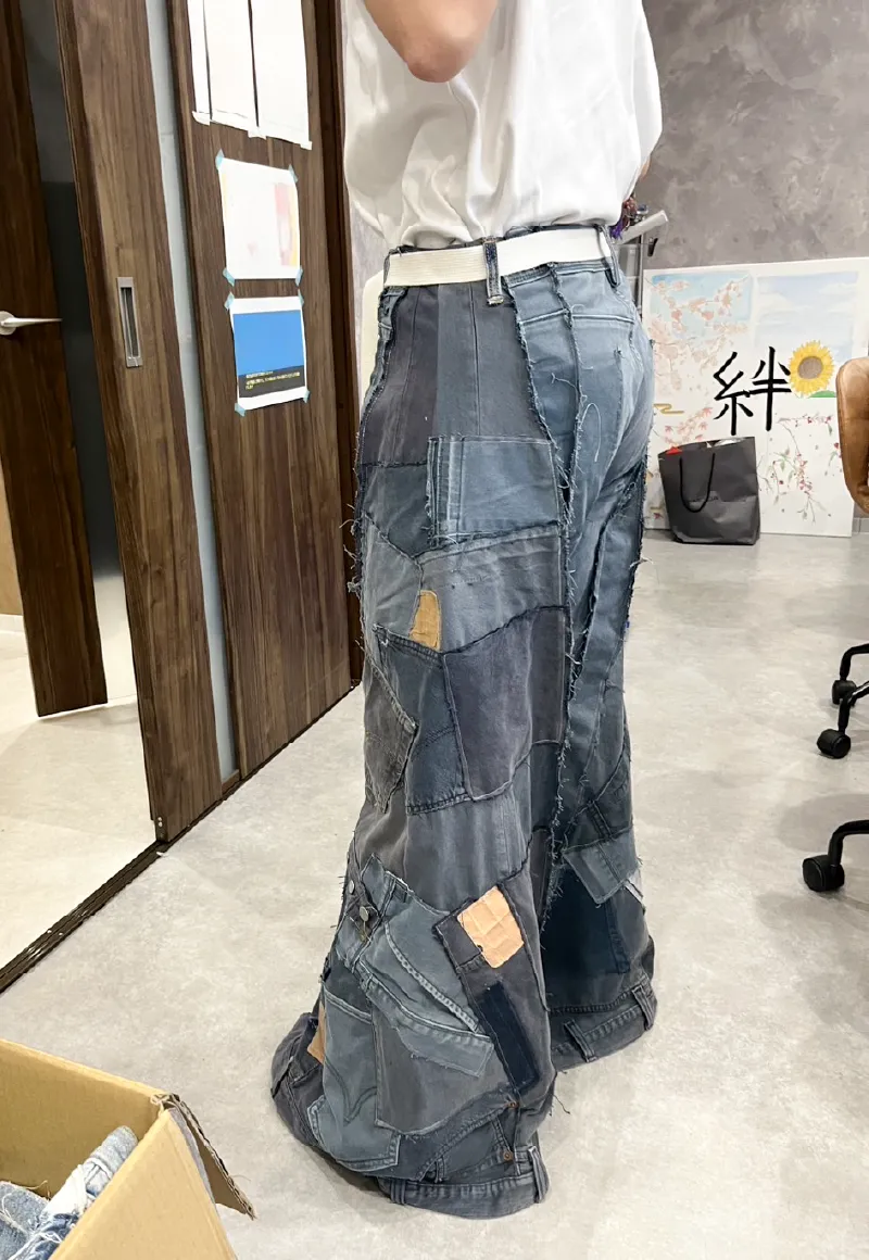 デニム生地をパッチワークで繋ぎ合わせた、ワイドシルエットのリメイクデニムパンツを試着している女性職員の側面全体像。ヒップポケットや膝下部分に異なる生地が配置されている。