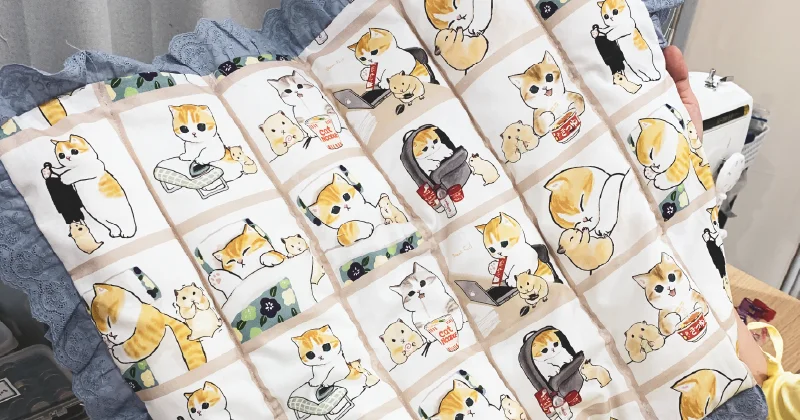 猫柄の猫用クッションの表面。イラストには日常を過ごす猫たちの姿が描かれており、ポップでユニークな雰囲気が漂う。